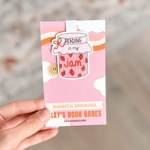 May include: Pink and orange magnetic bookmark with a cartoon illustration of a jar of strawberry jam with the text "Reading is my jam". The bookmark is labeled "Magnetic Bookmark Kay's Book Babes @kaysbookbabes"