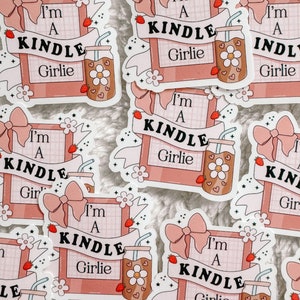 May include: A set of pink and white stickers with the text "I'm a Kindle Girlie" and a cartoon image of a drink with a straw and a flower. The stickers are decorated with pink bows, stars, and flowers.