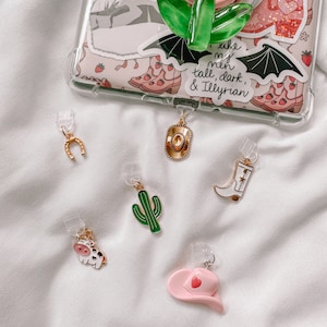 Puede incluir: Un conjunto de seis encantos que incluyen una herradura, un sombrero de vaquero, un cactus, una vaca, una bota y un sombrero de vaquero rosa con un corazón. Los encantos están unidos a clips de plástico transparente.