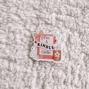 May include: A pink and white sticker with the text "I'm a Kindle Girlie" and a drawing of a book, a bow, a flower, and a glass of iced tea.