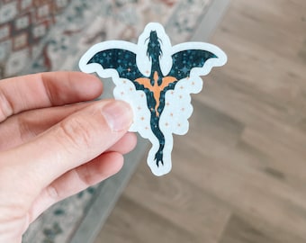 Pode incluir: Um adesivo de dragão preto e dourado com um fundo estrelado. O dragão está voando para cima com as asas abertas.