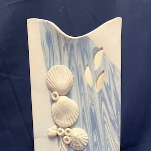 May include: A white ceramic vase with a blue and white marbled design. The vase has a raised design of seashells and seaweed.