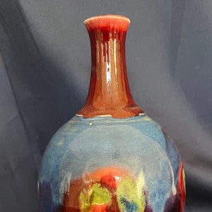 May include: A round ceramic vase with a narrow neck. The vase is decorated with a blue, red and green glaze. The glaze has a mottled effect, creating a unique and abstract design.