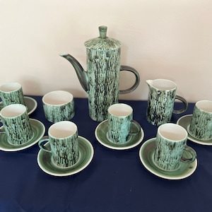 May include: A set of green and black ceramic coffee cups and a matching teapot. The cups and teapot have a textured, tree bark-like design.