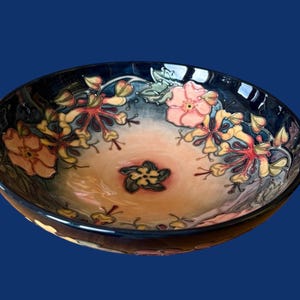 Könnte beinhalten: Dekorative Keramikschale mit dunkelblauem Rand und floralem Design. Das Innere zeigt rosa, gelbe und rote Blumen mit grünen Blättern auf hellorangefarbenem und blauem Hintergrund.