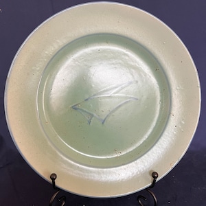 May include: A light green ceramic plate with a blue design in the center. The plate is on a black stand.