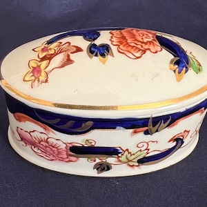 May include: Oval ceramic trinket box with a floral design in shades of blue, red, yellow, and green. The lid has a gold trim and a floral design.