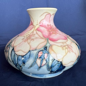 Puede incluir: Un jarrón grande de cerámica de color crema con un diseño floral. El jarrón presenta flores rosas, amarillas y azules con hojas verdes. El jarrón tiene una base ancha y un cuello estrecho.