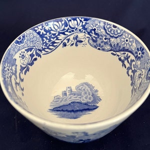 Könnte beinhalten: Eine weiße Keramikschale mit blauem Blumen- und Landschaftsdesign. Der Rand weist ein detailliertes blaues Blumenmuster auf, während das Innere eine blaue Landschaftsszene zeigt. Die Schale eignet sich zum Servieren von Speisen oder als dekoratives Stück.