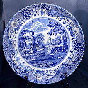 May include: Blue and white ceramic plate with a floral border and a central image of a landscape with a castle and a bridge.