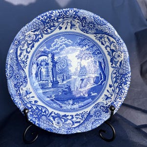 May include: A blue and white ceramic bowl with a floral pattern and a landscape scene in the centre. The bowl is on a black metal stand.