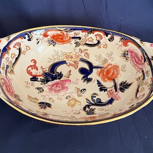 May include: A large oval serving bowl with a floral pattern in shades of blue, red, and gold. The bowl has two handles with holes on each side.