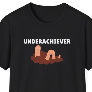 May include: Black t-shirt with the word "UNDERACHIEVER" in white block letters above a cartoon worm emerging from a brown mound. The worm is light brown with a smiling face.