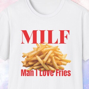 May include: White t-shirt with the word "MILF" in red block letters above a pile of golden-brown french fries. Below the fries, the text "Man I Love Fries" is printed in red.