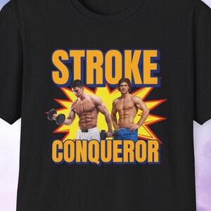 May include: Black t-shirt with a graphic of two muscular men and the words "STROKE CONQUEROR" in yellow and blue. The design includes a yellow burst behind the men.