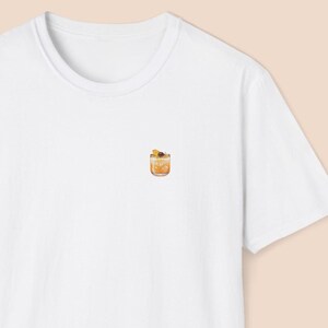 May include: White t-shirt with a small embroidered image of a cocktail glass with a slice of orange and a cherry.