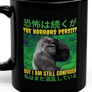 May include: Black ceramic mug featuring a gorilla image with the text "THE HORRORS PERSIST" in green and white. The mug also includes Japanese text. The mug has a curved handle.