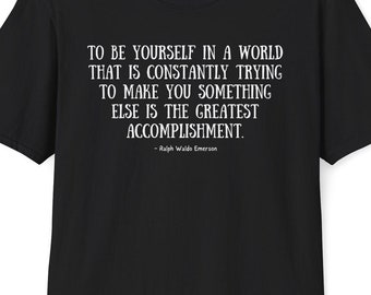 May include: Black t-shirt with white text. The text reads: "TO BE YOURSELF IN A WORLD THAT IS CONSTANTLY TRYING TO MAKE YOU SOMETHING ELSE IS THE GREATEST ACCOMPLISHMENT." Below the quote is "- Ralph Waldo Emerson."