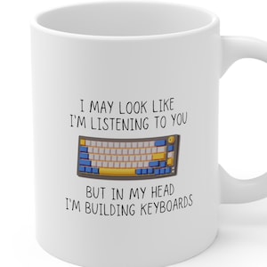 May include: White ceramic mug with a black and white graphic of a keyboard and the text "I may look like I'm listening to you but in my head I'm building keyboards."