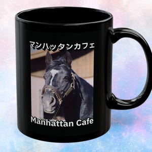 Puede incluir: Una taza de cerámica negra con una impresión fotográfica de un caballo oscuro con una mancha blanca en la cara, que lleva un cabestro de cuero marrón. El texto "マンハッタンカフェ" está impreso en blanco sobre el caballo y "Manhattan Cafe" debajo.