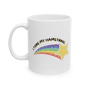 May include: White ceramic coffee mug with a rainbow shooting star and the text "I tore my hamstring".
