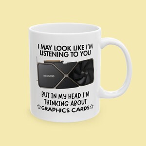 以下が含まれることがあります： 黒とシルバーのグラフィックカードのデザインと「I MAY LOOK LIKE I'M LISTENING TO YOU BUT IN MY HEAD I'M THINKING ABOUT GRAPHICS CARDS」というテキストが入った白いセラミックマグ。マグには湾曲したハンドルが付いています。