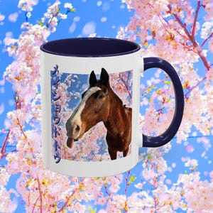 May include: White ceramic mug with a navy blue interior and handle. The mug features a brown horse with a white stripe on its face, set against a background of pink cherry blossoms and blue sky. Japanese text is printed on the side of the mug.