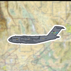 Puede incluir: Una pegatina con un avión de transporte militar C-17 Globemaster III gris. La pegatina incluye el texto "U.S. AIR FORCE" y otras marcas. El fondo es un mapa.