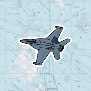 May include: A sticker of a grey fighter jet with black detailing, set against a light blue map background. The jet is shown from above, with detailed wings and engines. The sticker has a white border.