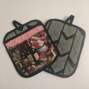 May include: Two black and white patterned oven mitts. One mitt features a colorful print of wine bottles, flowers, and fruit.