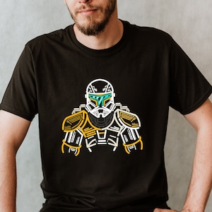 May include: A black t-shirt featuring a white and yellow outline of a Star Wars character wearing a helmet. The character has a blue visor.