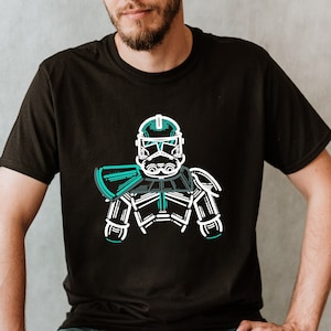 May include: A black t-shirt with a white outline of a Star Wars clone trooper helmet and armor. The helmet and armor are outlined in teal.
