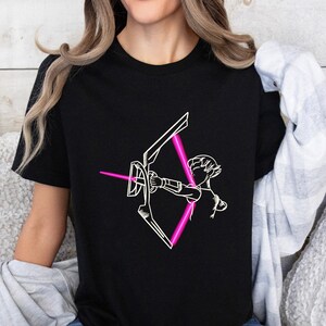 Könnte beinhalten: Ein schwarzes T-Shirt mit einer weißen Umrandung einer Person, die einen Bogen und Pfeil hält. Der Pfeil ist leuchtend pink.