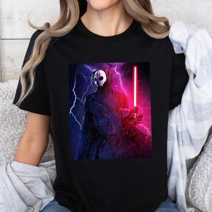 Könnte beinhalten: Ein schwarzes T-Shirt mit einem Grafikdruck einer maskierten Figur, die ein Lichtschwert in einer dunklen und stürmischen Umgebung hält.