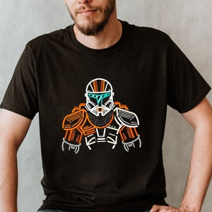 May include: A black t-shirt featuring a white outline of a futuristic soldier wearing an orange and white helmet. The soldier is wearing armour with orange accents.