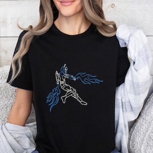 Może przedstawiać: Czarny t-shirt z białym rysunkiem postaci z niebieskimi płomieniami na czarnym tle.