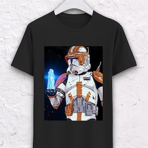 May include: Black t-shirt with a graphic of a Star Wars clone trooper holding a blue energy blade. The clone trooper is wearing orange and white armor.