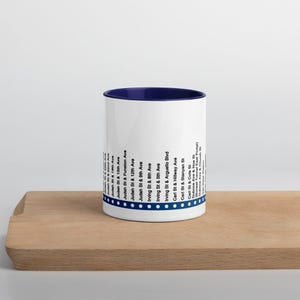 May include: White ceramic mug with a blue rim and a list of street names and intersections printed on the side. The text includes "Judah St & 19th Ave", "Judah St & 15th Ave", "Judah St & Funston Ave", "Judah St & 12th Ave", "Judah St & 9th Ave", "Irving St & 8th Ave", "Irving St & 5th Ave", "Irving St & Arguello Blvd", "Carl St & Hillway Ave", "Carl St & Stanyan St", "Carl St & Cole St", "Duboce Ave & Noe St", "(Sunset Tunnel East Portal)", "Duboce Ave & Church", and "Van Ness Ave".