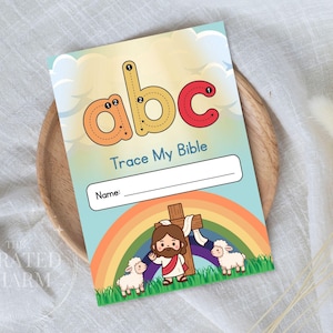 Puede incluir: Un cuaderno de actividades infantiles con el texto "Trace My Bible" y las letras "abc" en naranja y rojo. La portada presenta una ilustración de Jesús, un arcoíris y dos corderos.