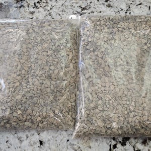 May include: Two rectangular clear plastic bags filled with small, angular, light brown and tan stone chips. The bags are sealed at the top and contain a uniform mixture of crushed rock fragments that appear to be of a similar size and texture.