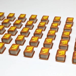 Może przedstawiać: Kolekcja miniaturowych książek z brązowymi okładkami i żółtymi akcentami. Książki ułożone są w równych rzędach na białej powierzchni, sugerując motyw edukacji lub literatury. Książki są małe i szczegółowe.