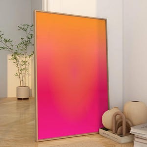 May include: A framed art print with a vibrant gradient of orange, red, and pink hues. The artwork leans against a white wall, complemented by neutral-toned decor, including a beige rug, a sofa, and decorative vases.
