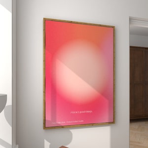 Può includere: Una stampa d'arte astratta incorniciata con uno sfondo sfumato rosa e arancione e un cerchio bianco al centro. Il testo "attract good things" è stampato in bianco nella parte inferiore della stampa.