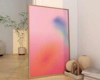 May include: A framed abstract painting with a pink, orange, and blue gradient. The painting is hanging on a white wall in a room with wooden floors and a rug. There are also some decorative objects on the floor, including a vase and a stack of books.