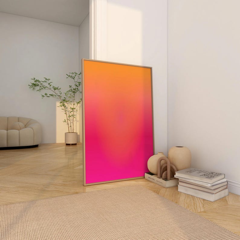 May include: A framed art print with a vibrant gradient of orange, red, and pink hues. The artwork leans against a white wall, complemented by neutral-toned decor, including a beige rug, a sofa, and decorative vases.