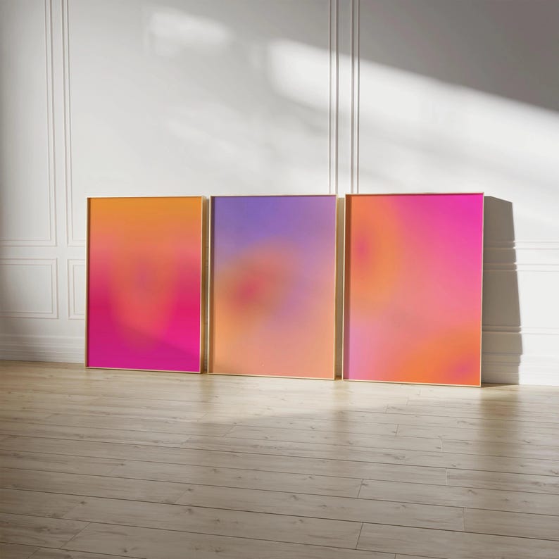 May include: Three framed abstract art prints with a gradient of colors. The frames have a gold finish. The color gradients are orange to pink, purple to orange, and pink to orange.