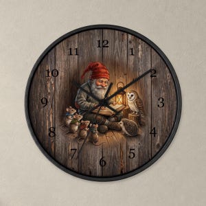 May include: A round wall clock with a black frame and a wood-plank background. The face features an illustration of a gnome reading a book to a group of mice, a hedgehog, and an owl by lantern light. Black numbers mark the hours.