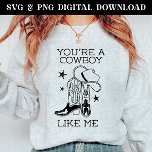 May include: A gray sweatshirt with the text "You're a Cowboy Like Me" in black. The design includes a pair of cowboy boots and a cowboy hat.