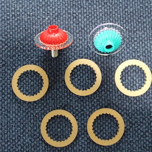 May include: A set of hardware components including one red and one teal fluted plastic cap, each attached to a clear circular disc, and five gold-colored metal washers with serrated inner edges arranged in a triangular formation below the caps.