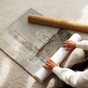 May include: An abstract art print with neutral tones of gray, white, and beige. A rolled-up print and a cardboard tube are next to the artwork. The image is taken from an overhead perspective.